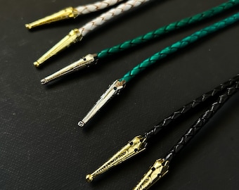 May include: Five different bolo ties with various colored braided cords and silver and gold tips. The bolo ties are arranged in a row on a black surface.