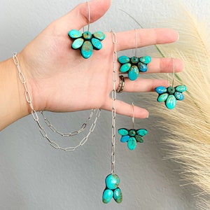 Pode incluir: Um conjunto de joias com brincos e um colar de pedra turquesa. Os brincos e o pendente t&ecirc;m um design floral, com detalhes em metal prateado. O colar tem um design de elos de corrente.