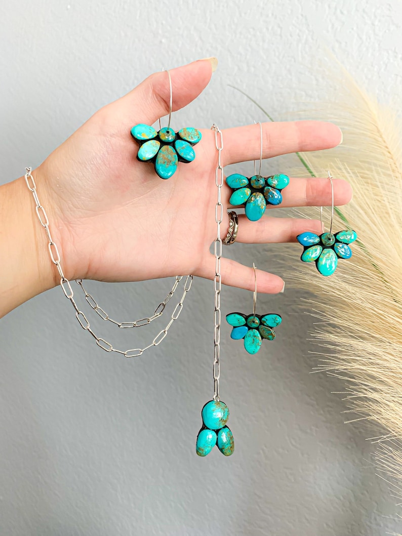 Pode incluir: Um conjunto de joias com brincos e um colar de pedra turquesa. Os brincos e o pendente t&ecirc;m um design floral, com detalhes em metal prateado. O colar tem um design de elos de corrente.