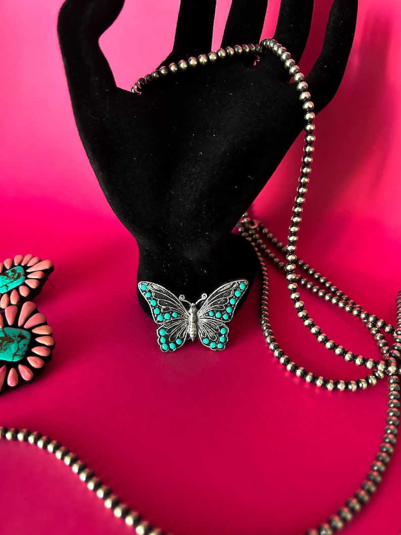 May include: A silver chain necklace with turquoise butterfly pendant on a pink background.