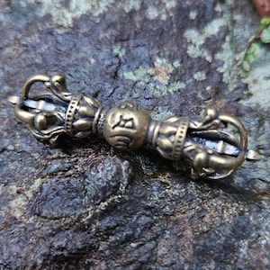 Puede incluir: Un pequeño y ornamentado molinillo de oración de mano de latón con un centro esférico y detalles intrincados. La rueda está diseñada para girar para la meditación y la oración.