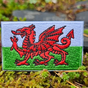 Può includere: Toppa ricamata con la bandiera gallese. Presenta un drago rosso su sfondo verde e bianco. La toppa rettangolare ha un bordo cucito. Il drago è dettagliato con contorni neri.