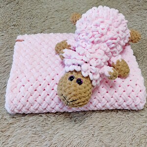 Peut inclure: Une couverture en crochet rose avec un jouet en crochet d'agneau rose et brun sur le dessus.
