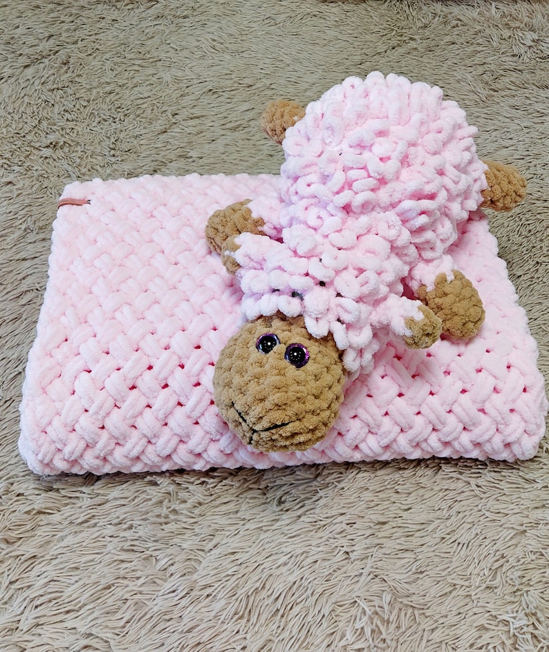 Peut inclure: Une couverture en crochet rose avec un jouet en crochet d'agneau rose et brun sur le dessus.