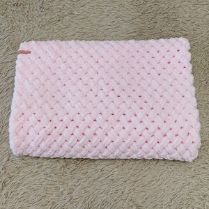 Peut inclure: Une couverture en tricot rose avec un motif en chevron. La couverture est faite d'un fil doux et moelleux.