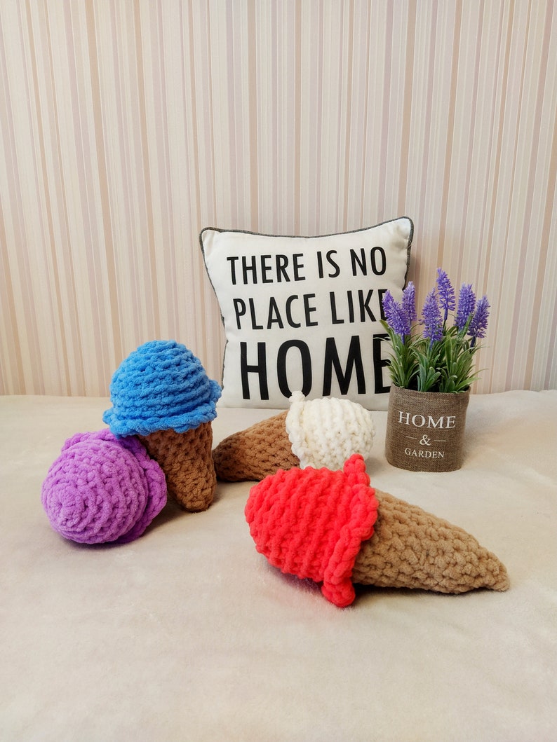 Peut inclure: Quatre c&ocirc;nes de cr&egrave;me glac&eacute;e en crochet de diff&eacute;rentes couleurs&nbsp;: violet, bleu, blanc et rouge. Les c&ocirc;nes sont pos&eacute;s sur une surface blanche et moelleuse. Un coussin avec le texte &laquo;&nbsp;Il n&rsquo;y a pas de place comme &agrave; la maison&nbsp;&raquo; se trouve en arri&egrave;re-plan.