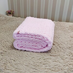 Peut inclure: Une couverture en tricot rose pli&eacute;e sur une surface moelleuse brun clair.
