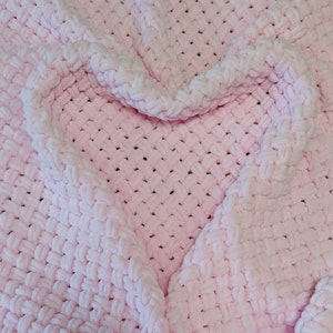 Peut inclure: Une couverture en crochet rose avec une forme de c&oelig;ur form&eacute;e par les plis du tissu.