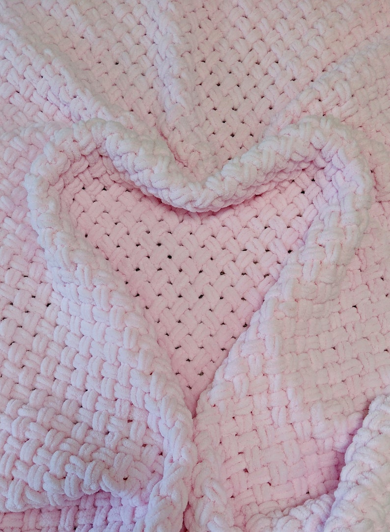 Peut inclure: Une couverture en crochet rose avec une forme de c&oelig;ur form&eacute;e par les plis du tissu.