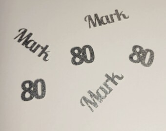 May include: Silver glitter confetti with the name "Mark" and the number "80" repeated four times.