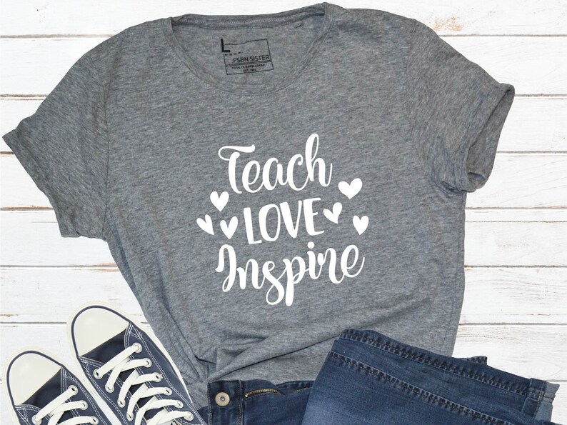 May include: A heather grey t-shirt with the text "Teach Love Inspire" in white lettering with small white hearts around the text.