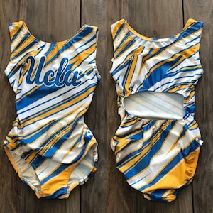 May include: A pair of white, blue, and yellow leotards with a cut-out back. The leotard on the left has the word "UCLA" written in blue on the front.