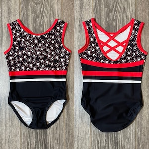 May include: Black and red gymnastics leotard with a white stripe and a pattern of white and red letters. The leotard has a criss-cross back design.