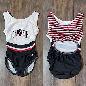 May include: Two black and white leotards with red accents. One leotard has the text "Ohio State" on the front. The other leotard has a striped pattern.