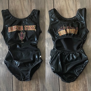 Peut inclure: Deux justaucorps noirs avec un dos découpé. Un justaucorps a "Arizona State" et un graphique d'une lance avec un soleil dessus. L'autre justaucorps a "Sun Devils" en lettres dorées.