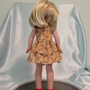 Puede incluir: Una mu&ntilde;eca con un vestido marr&oacute;n y amarillo con estampado de hojas. El vestido tiene una falda con volantes. La mu&ntilde;eca lleva zapatos rojos.