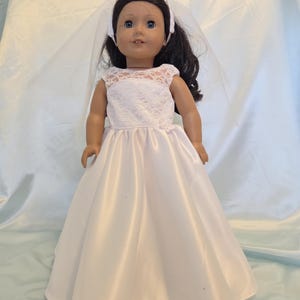 May include: A doll wearing a white satin wedding dress with a lace bodice and a matching veil. The doll has dark hair and blue eyes, and is posed against a light blue background.
