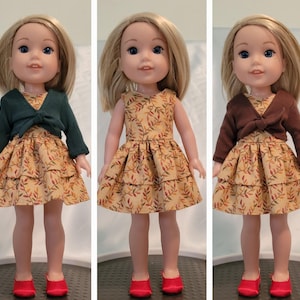 Puede incluir: Tres mu&ntilde;ecas con vestidos de tem&aacute;tica oto&ntilde;al con estampados de hojas. Cada mu&ntilde;eca lleva un c&aacute;rdigan de un color diferente, uno verde, uno marr&oacute;n y uno sin c&aacute;rdigan. Todas las mu&ntilde;ecas llevan zapatos rojos.