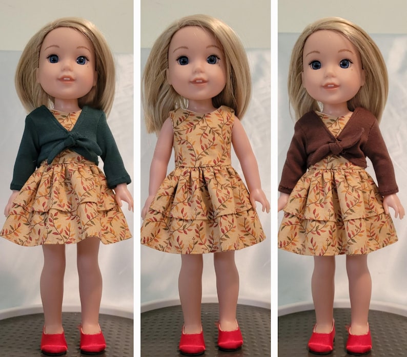 Puede incluir: Tres mu&ntilde;ecas con vestidos de tem&aacute;tica oto&ntilde;al con estampados de hojas. Cada mu&ntilde;eca lleva un c&aacute;rdigan de un color diferente, uno verde, uno marr&oacute;n y uno sin c&aacute;rdigan. Todas las mu&ntilde;ecas llevan zapatos rojos.