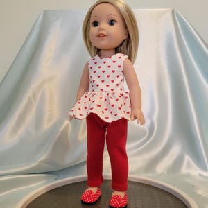 May include: A doll wearing a white dress with red hearts and red pants with red and white polka dot shoes.