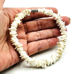 May include: White shell bracelet with a silver clasp. The bracelet is made of small, flat pieces of shell that are strung together.