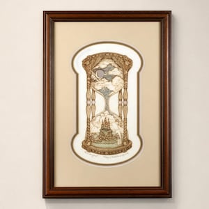 May include: A framed artwork depicting an hourglass with a detailed, whimsical design. The hourglass features a landscape with clouds, a moon, and a castle. The frame is dark brown, and the artwork is displayed on a white wall.