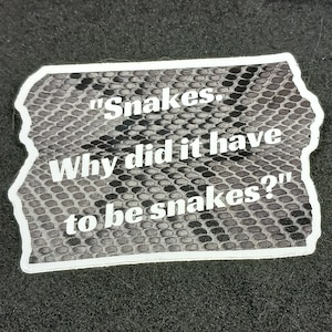 May include: A white sticker with a snake skin pattern and the text "Snakes. Why did it have to be snakes?"