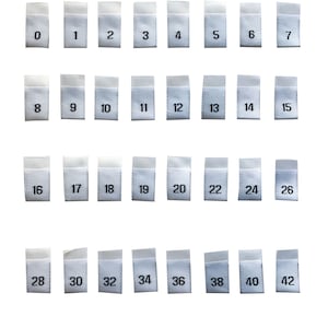 以下が含まれることがあります： 白い布製のサイズラベルに、黒い数字が0から42まで書かれています。ラベルは4行8列に並んでいます。