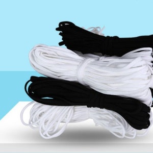 Puede incluir: Dos carretes de cordón elástico, uno negro y uno blanco. Los carretes están apilados uno encima del otro.