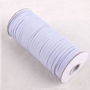 May include: A roll of white elastic cord wound around a cardboard spool. The elastic cord is used for sewing and crafting projects.