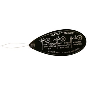 Könnte beinhalten: Schwarzer Plastik-Nähfaden-Einfädler mit einer weißen Metallschlaufe. Der Einfädler enthält Anweisungen zur Verwendung: "Push threader thru needle eye. Pass thread thru loop of threader. Withdraw threader. Can be used on sewing machines."