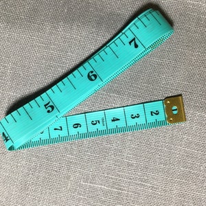 May include: A turquoise measuring tape with black markings and a gold metal end cap. The tape is marked with numbers from 2 to 7.