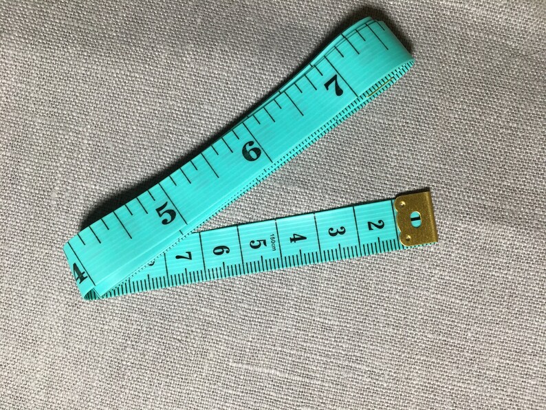 May include: A turquoise measuring tape with black markings and a gold metal end cap. The tape is marked with numbers from 2 to 7.