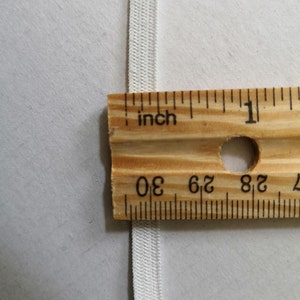May include: White elastic band measured with a ruler, showing it is 1/2 inch wide.