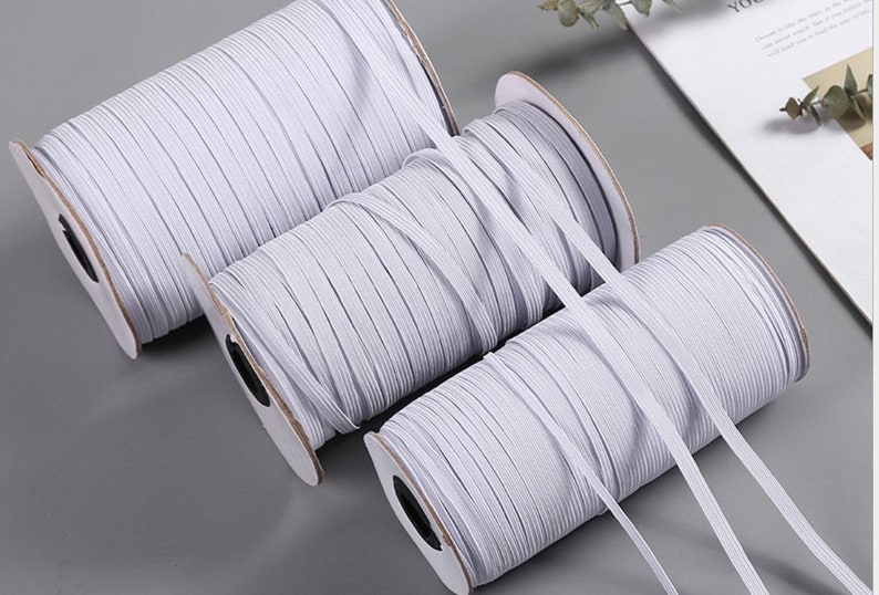 May include: Three spools of white elastic cord, wound on cardboard spools with black labels. The elastic cord is a popular material for crafting and sewing projects.
