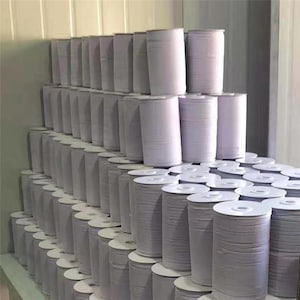 May include: A large stack of white spools of elastic thread. The spools are arranged in rows and columns, creating a uniform pattern.