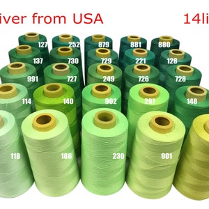 May include: A collection of 14 spools of green thread, ranging in shades from dark green to light green. The spools are arranged in a semi-circle, with the darkest green spools at the top and the lightest green spools at the bottom. Each spool has a yellow label with a number printed on it.