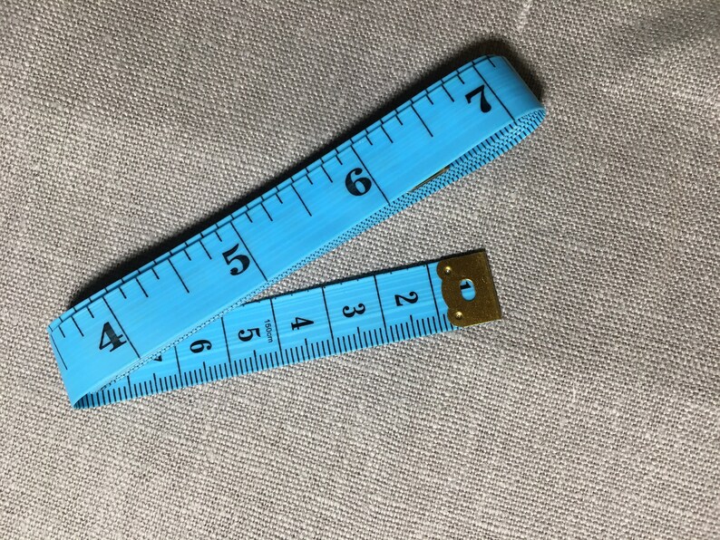 May include: A blue measuring tape with black numbers from 2 to 7. The tape is folded in half and the end is secured with a gold metal clasp.
