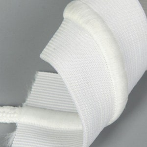 May include: White curtain tape with a soft, fuzzy trim. The tape is folded and rolled up, showing the texture of the fabric.