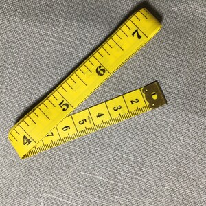 May include: A yellow measuring tape with black numbers, folded in half. The tape is marked in inches.