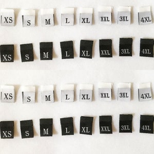 Op de afbeelding: Een set van 10 zwarte en witte stoffen labels met verschillende maten erop gedrukt: F, XS, S, M, L, XL, XXL, 3XL, 4XL en 5XL.