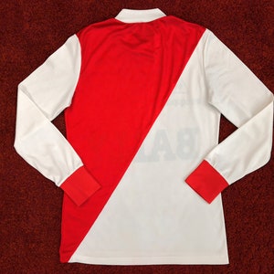 May include: A white and red long-sleeved jersey with a diagonal red stripe. The jersey has a white collar and red trim on the sleeves. The number "8" is printed on the back of the jersey.