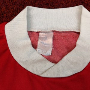 May include: Red and white long-sleeved shirt with a white ribbed collar and a white tag that reads "adidas" and "100% Cotton".