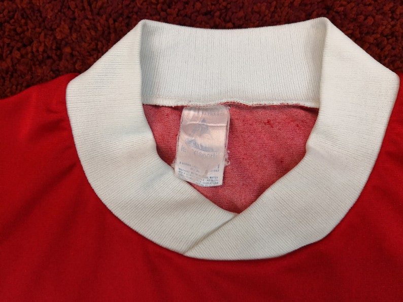 May include: Red and white long-sleeved shirt with a white ribbed collar and a white tag that reads "adidas" and "100% Cotton".