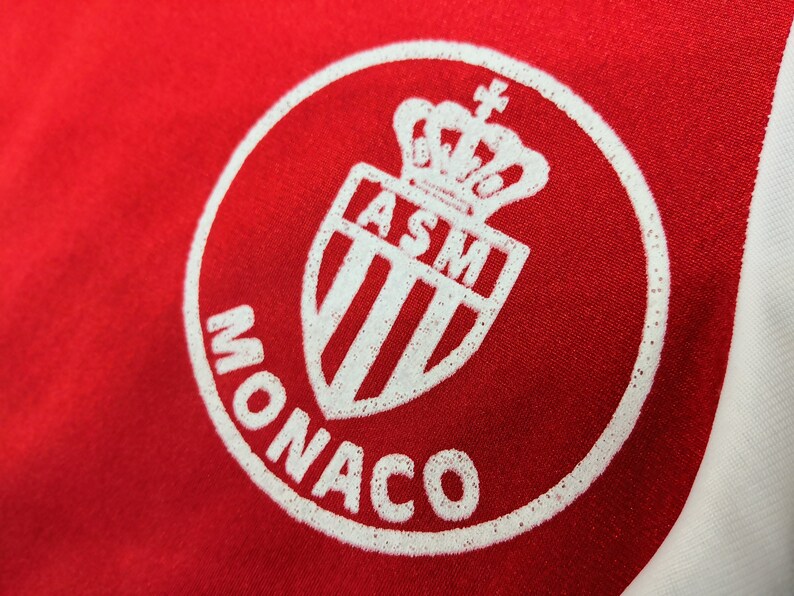 May include: White and red circular logo with the text "MONACO" and a white shield with a crown and the letters "ASM" inside.
