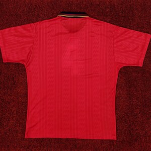 May include: A red short-sleeved polo shirt with a ribbed texture. The shirt has a black and gold collar.