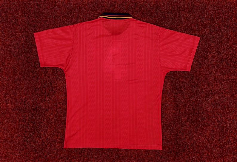 May include: A red short-sleeved polo shirt with a ribbed texture. The shirt has a black and gold collar.