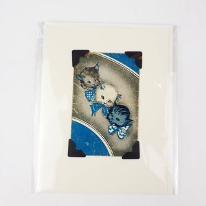 Puede incluir: Impresi&oacute;n vintage con tres caras de gatitos con lazos azules, sobre un fondo azul y gris. La impresi&oacute;n est&aacute; montada en una tarjeta blanca y asegurada con esquinas fotogr&aacute;ficas negras, en una funda de pl&aacute;stico transparente.
