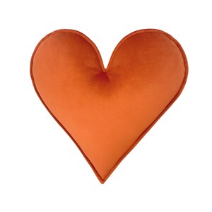 May include: A large, orange heart-shaped pillow. The pillow is made of a soft, plush fabric.