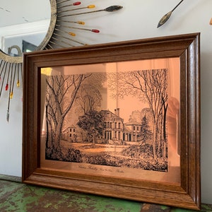 Op de afbeelding: Een ingelijste kopergravure van een historisch huis, "Castleton Bollinley, nabij Knutsford, Cheshire", in een houten lijst.